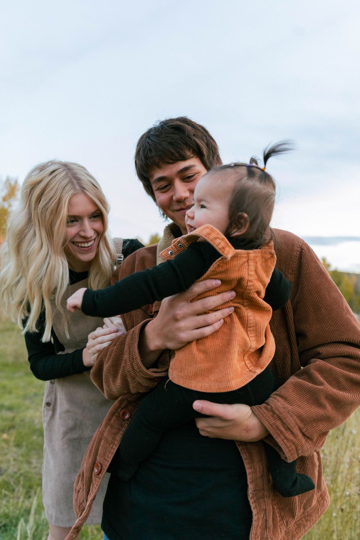 Parents holding their baby together in a sunlit field