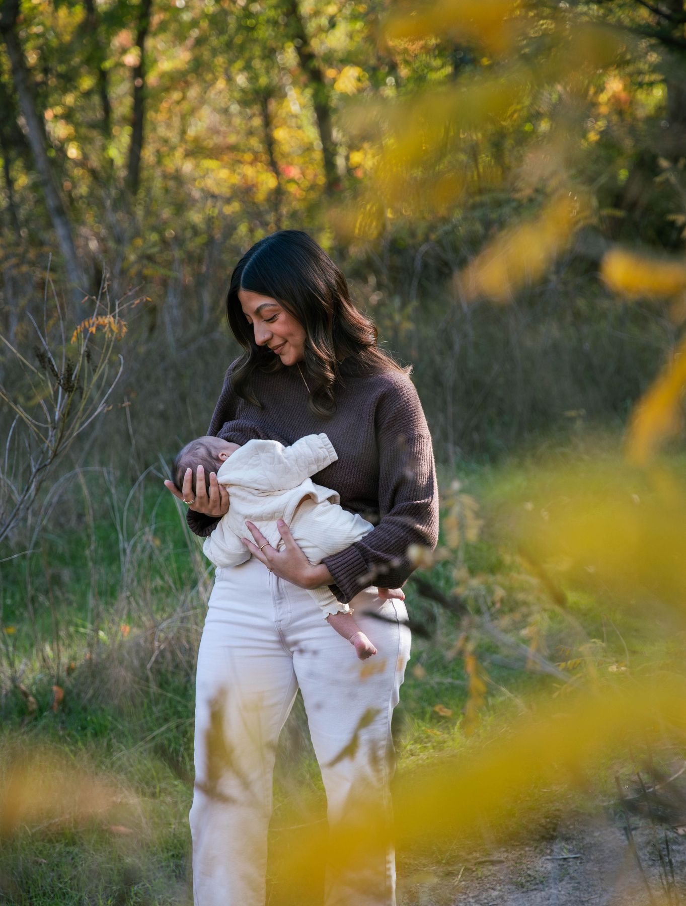 A mother and her newborn through the autumn leaves