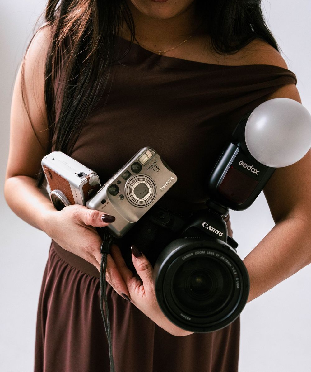 Lyka in a brown dress holding her cameras