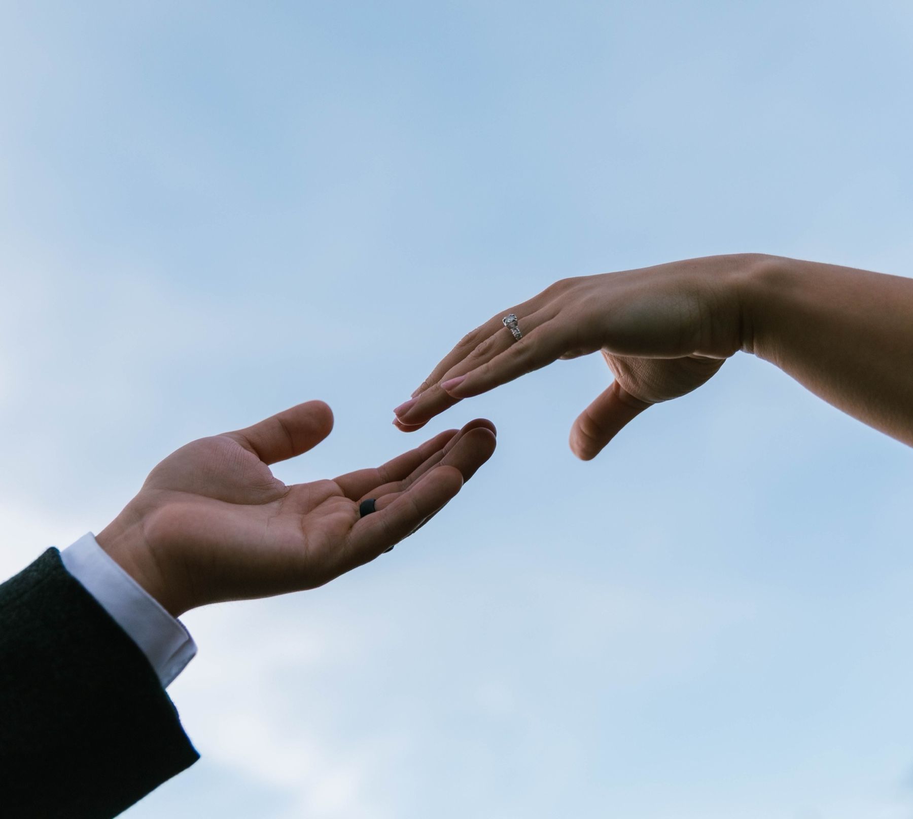 Two hands reaching toward each other against the sky